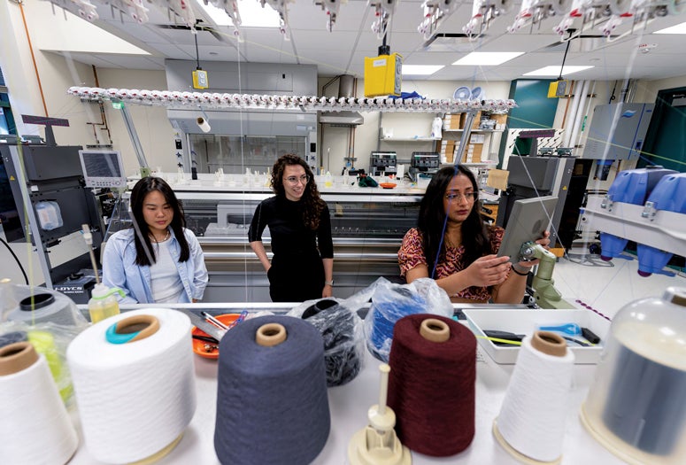 Photo of a lab with students and spools of thread in the foreground