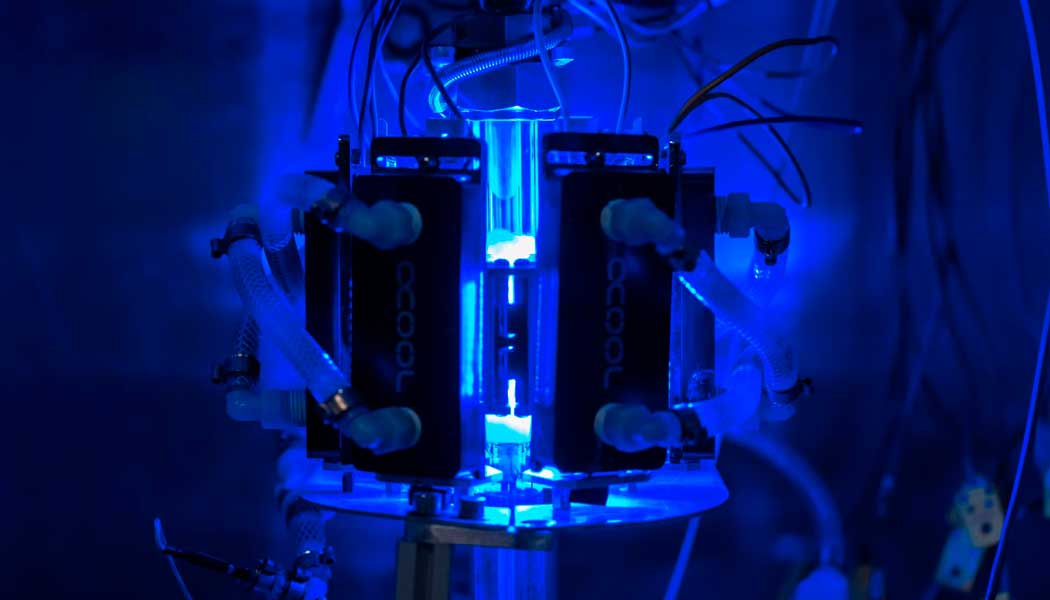 Photo of a Syzygy photoreactor in a dark lab with blue lighting