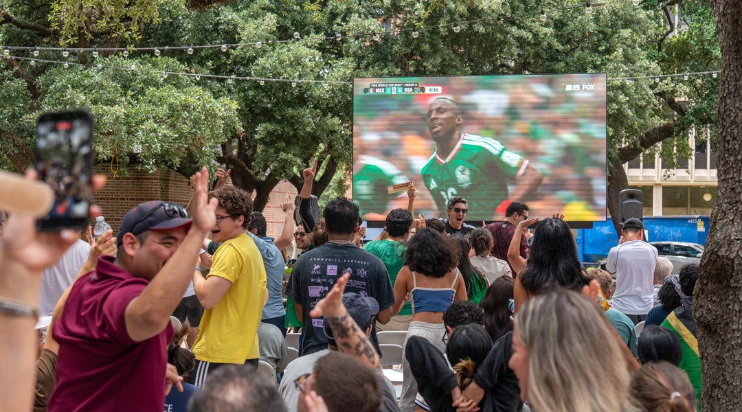 Photo of watch party outside in the courtyard of Valhalla with fans cheering for Mexico in front of a large tv screen showing the game
