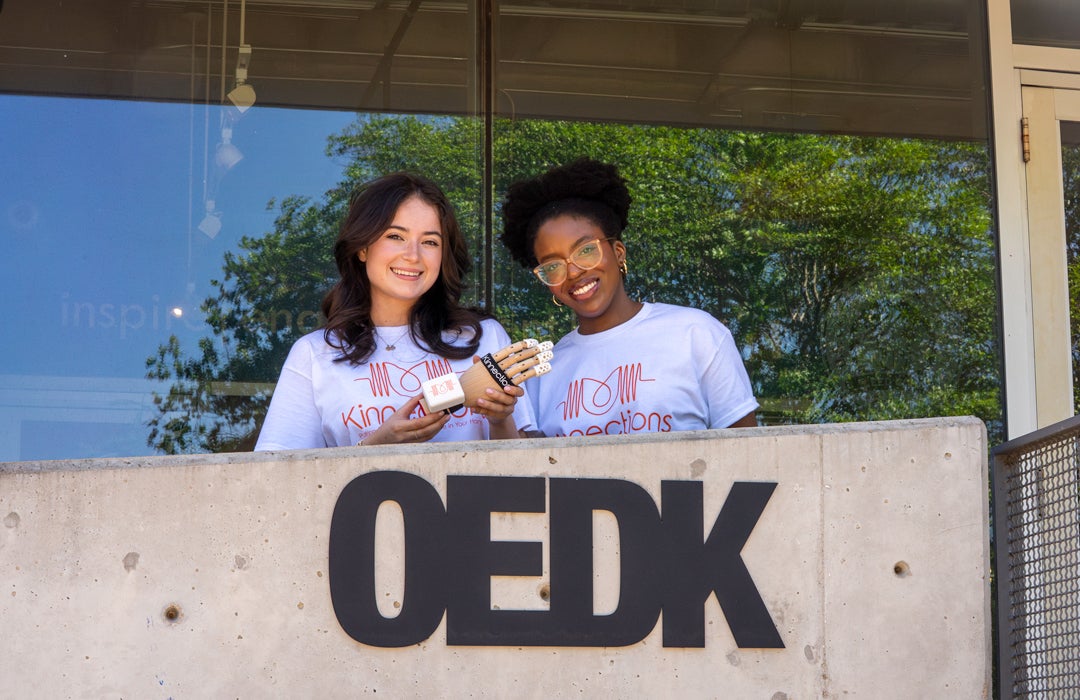 Photo of 2 students in front of the OEDK entrance holding their prototype glove