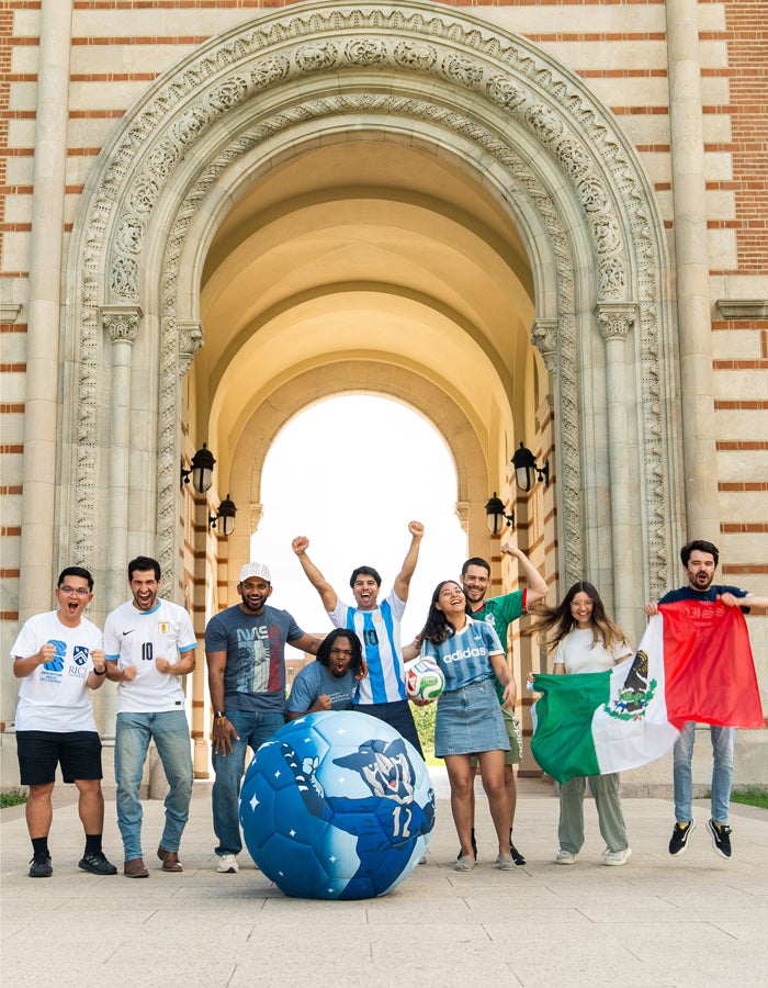 Photo of Fulbright grad students in front of Sallyport behind a large soccer ball that has Sammy painted on the ball. The students are sporting World Cup gear