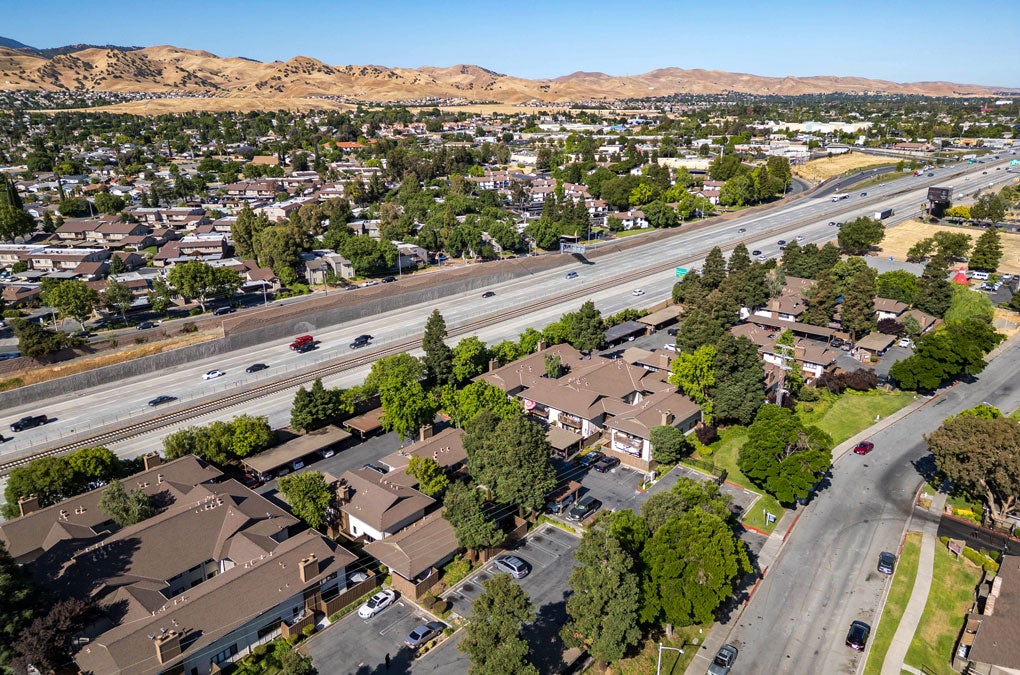 Aerial view of residential apartment complexes adjacent to Highway 4 with surrounding neighborhoods and the rolling hills of Antioch in the distance. 