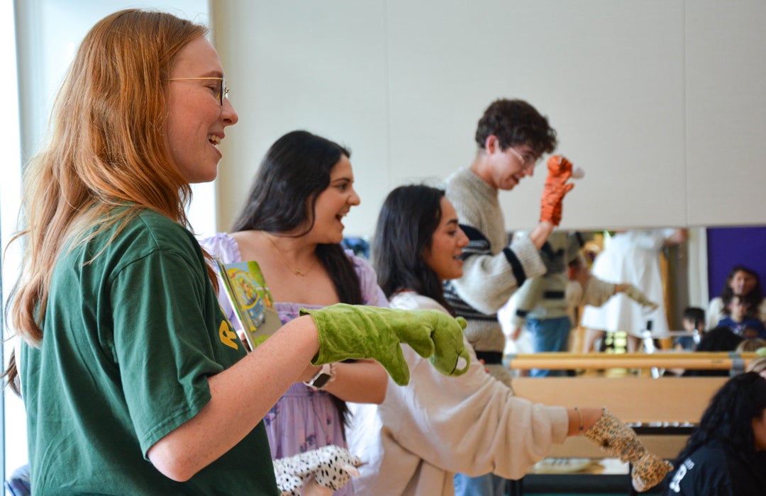 Photo of Rice students with Lucia Noto in the middle reading a book to students with puppets