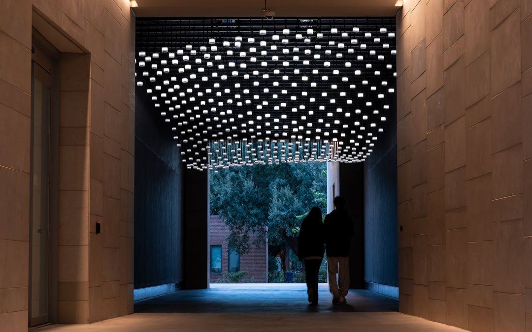 Photo of Climate Parliament with hybrid speaker-lights suspended from the ceiling of an enclosed exterior passageway 