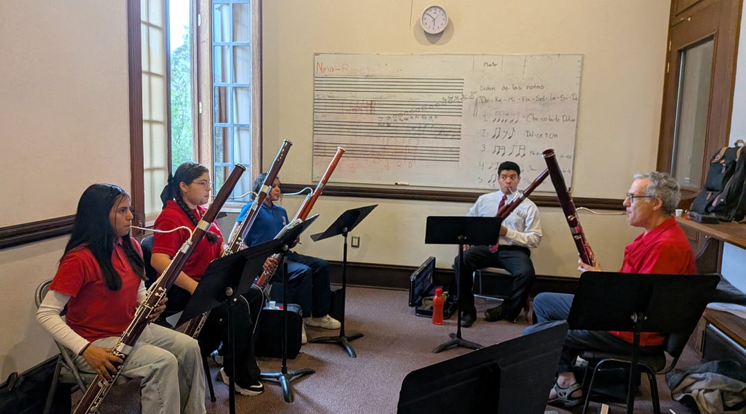 Photo of a Benjamin Kamins, professor of bassoon, in a room playing the bassoon among other bassoon students
