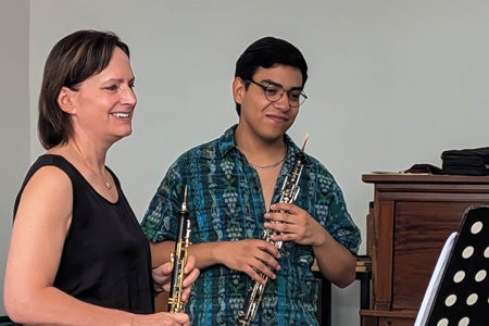 Photo of Erin Hannigan, professor of oboe, holding an oboe and instructing a student playing the oboe.