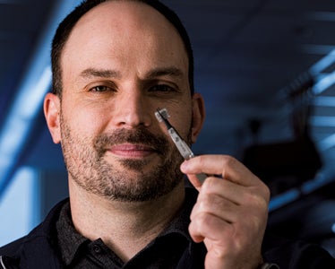 Photo of Jacob Robinson holding with pliers a wireless, battery-free brain stimulator