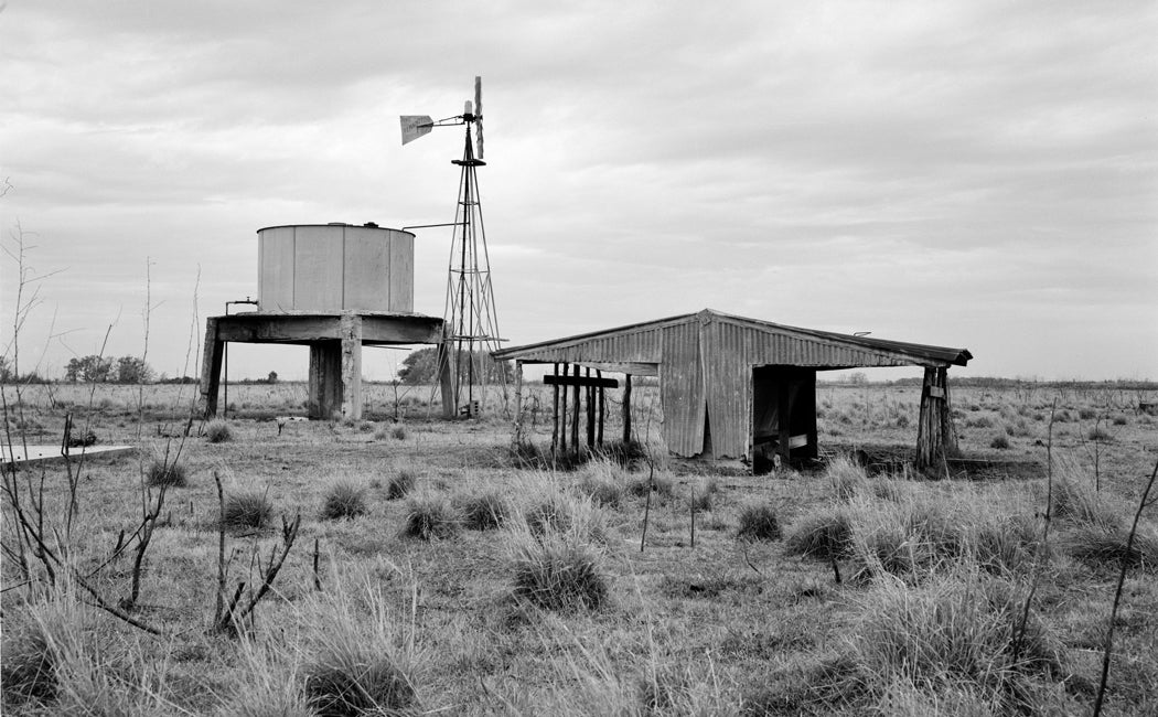 Black and white archival photo of Johnson Space Center in 1962 as farmland with windmill, water tank and shed in view