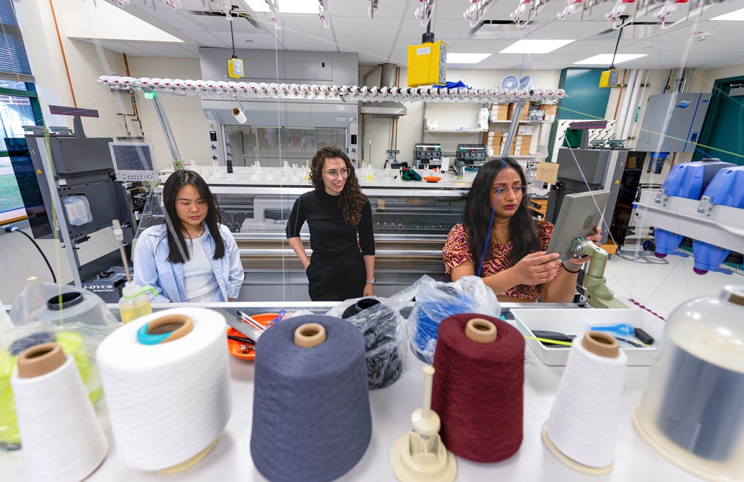 Photo of Texlab with spools of thread in the foreground and people working on a textile