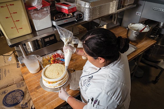 Chef Millan pipes icing onto a tres leches cake in the West Servery kitchen. Photo by Brandon Martin