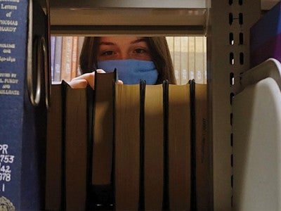 Female student wearing mask looking in library stacks