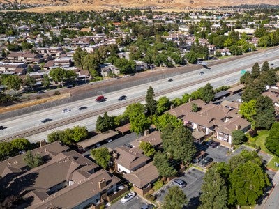 Aerial view of residential apartment complexes adjacent to Highway 4 with surrounding neighborhoods and the rolling hills of Antioch in the distance. 