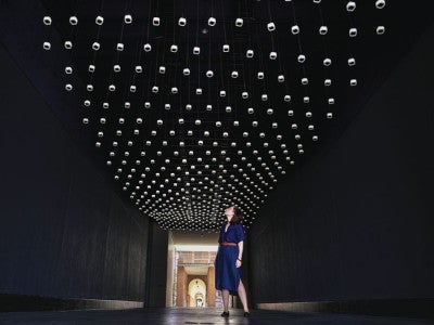 Photo of Climate Parliament with hybrid speaker-lights suspended from the ceiling of an enclosed exterior passageway 