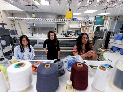 Photo of a lab with students and spools of thread in the foreground