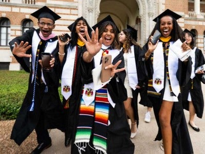 Photo of recently graduated students wearing cap and gown and celebrating with the Sallyport in the background