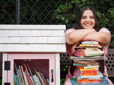 Photo of Lucia Noto next to a Little Library